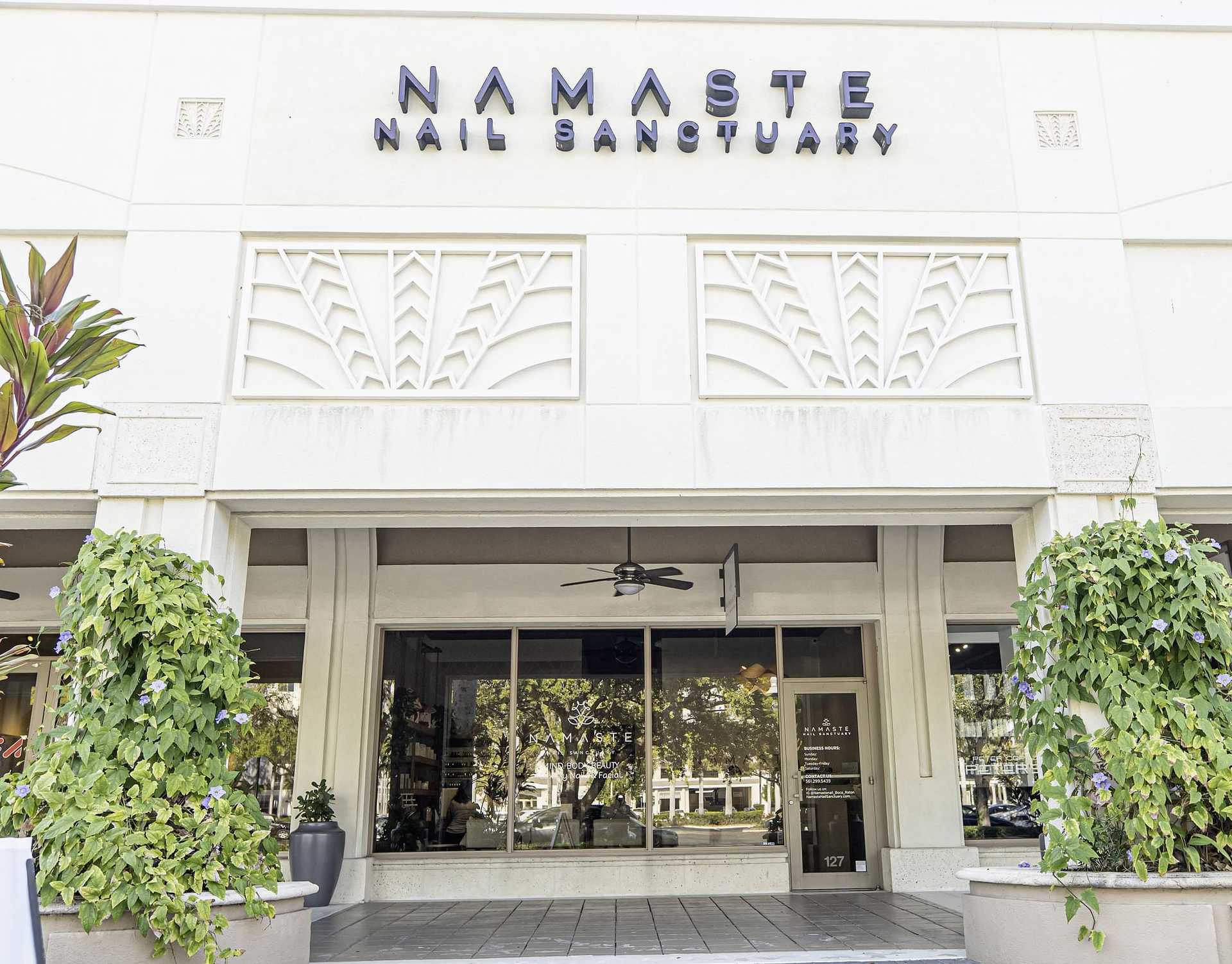 Nail salon entrance with greenery and modern signage reading 'Namaste Nail Sanctuary'.