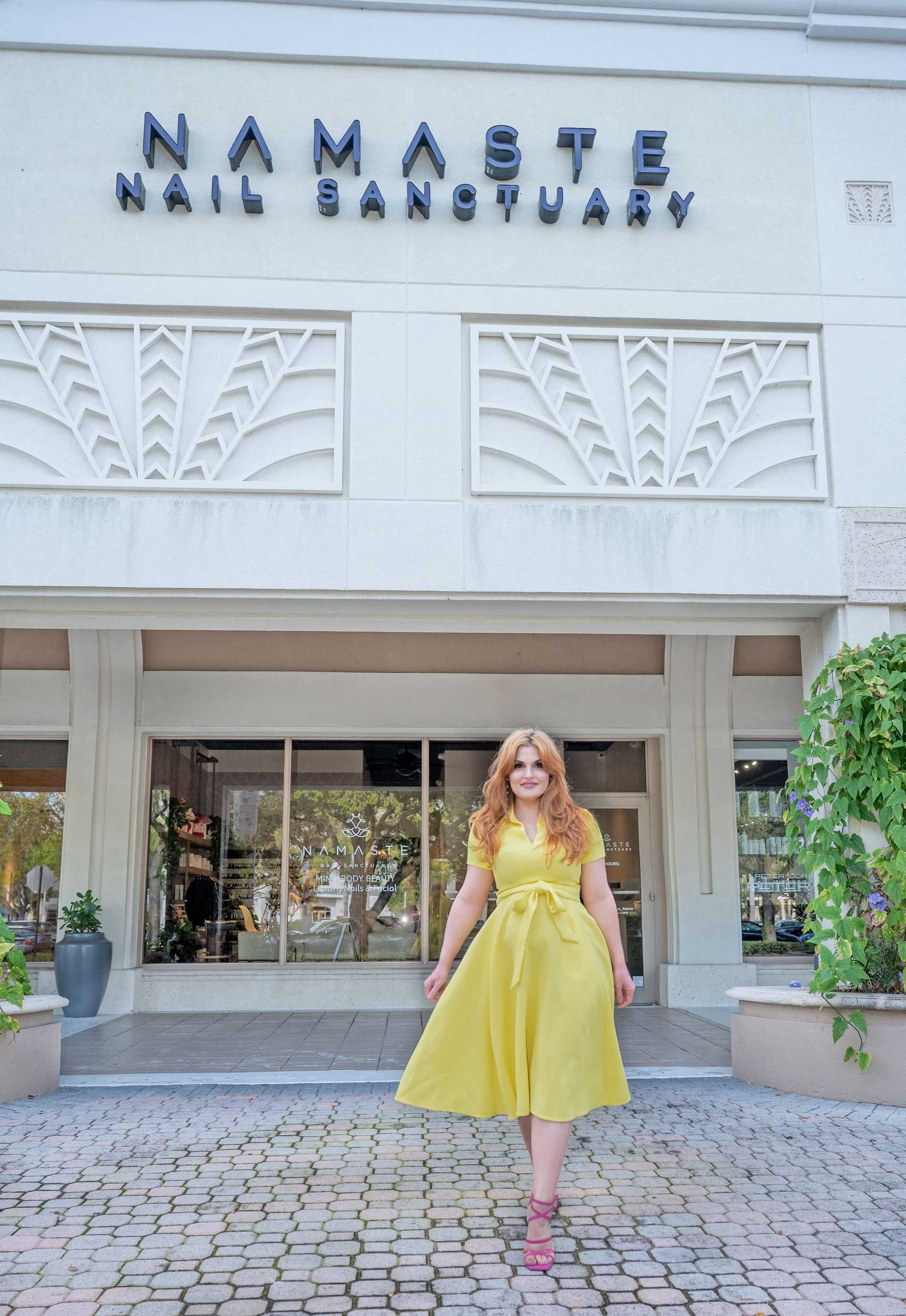 Woman in a yellow dress stands outside Namaste Nail Sanctuary entrance.