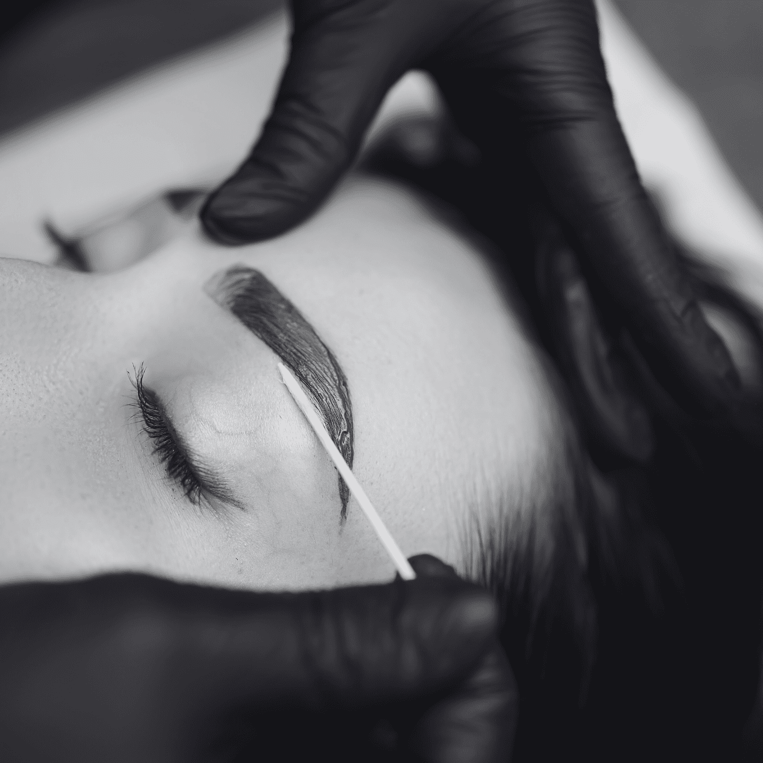 Eyebrow grooming using a cotton swab, person wears black gloves, close-up view.