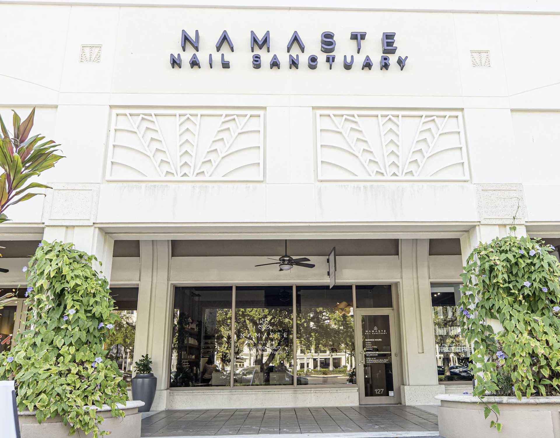 Nail salon entrance with greenery and modern signage reading 'Namaste Nail Sanctuary'.